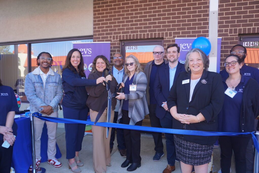 JEVS Human Services CEO flanked by SVP of Home Care Katie Brooks and Senior Director of Home Care Beverly Ward are surrounded by attendees as they cut the ribbon to officially open JEVS Care at Home's Dover, DE office